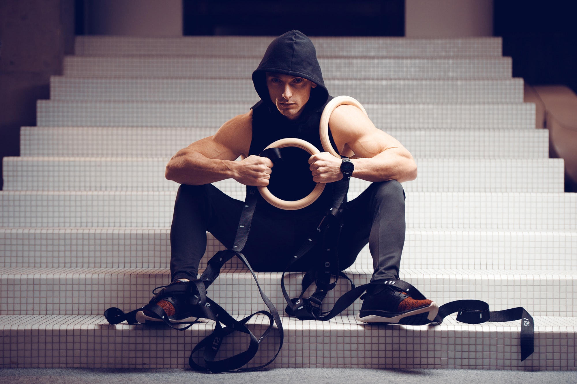 A young athletic gimnast sits on the steps of the gym and holds gymnastic rings