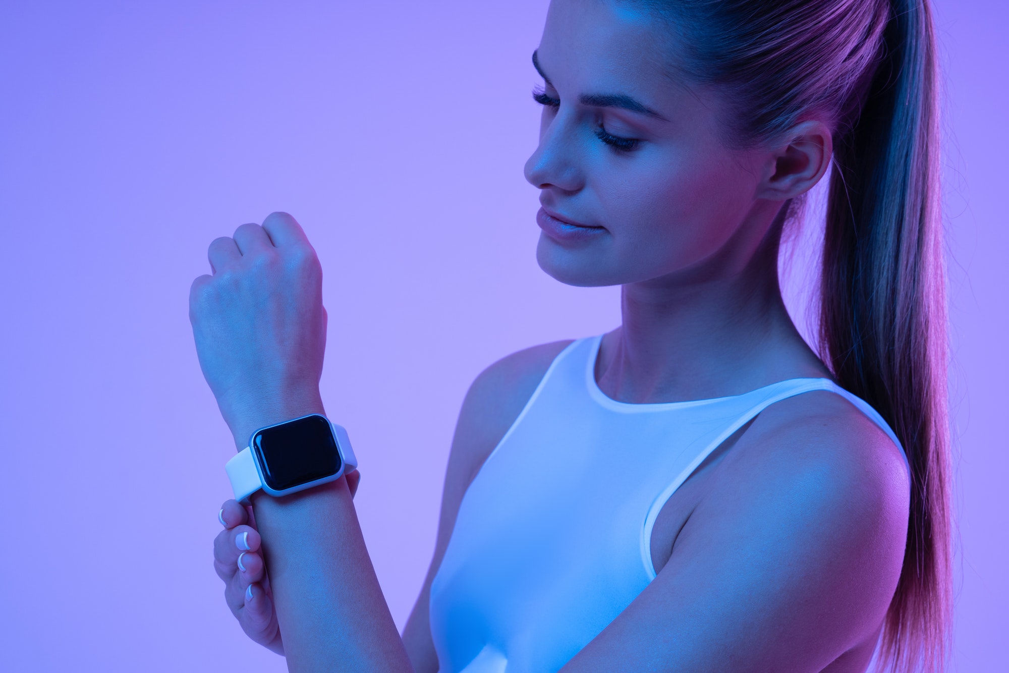 Happy sporty woman in neon light checking pulse and calories on smart fitness tracker