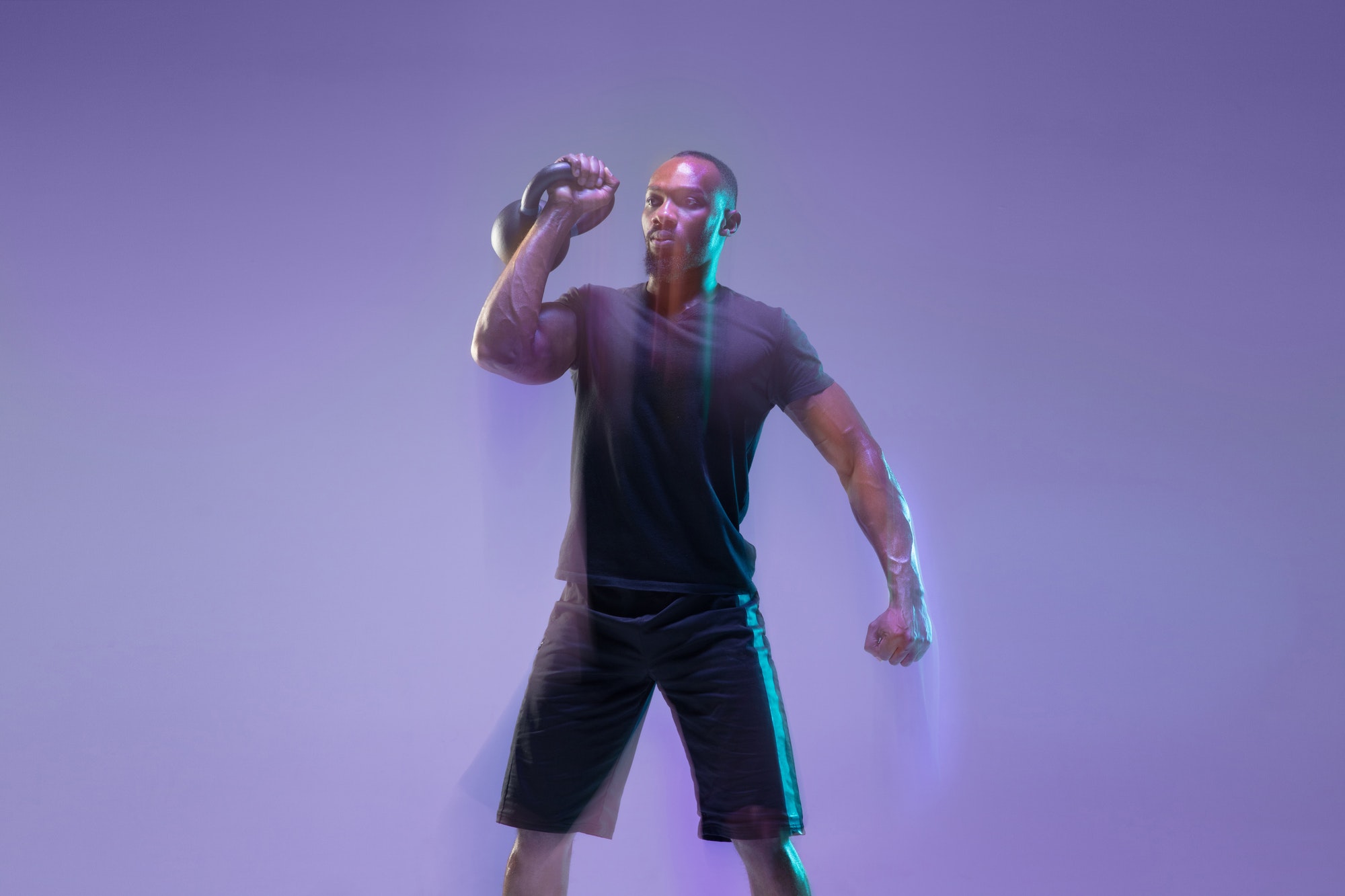 Young african-american bodybuilder training over purple background in neon, mixed light